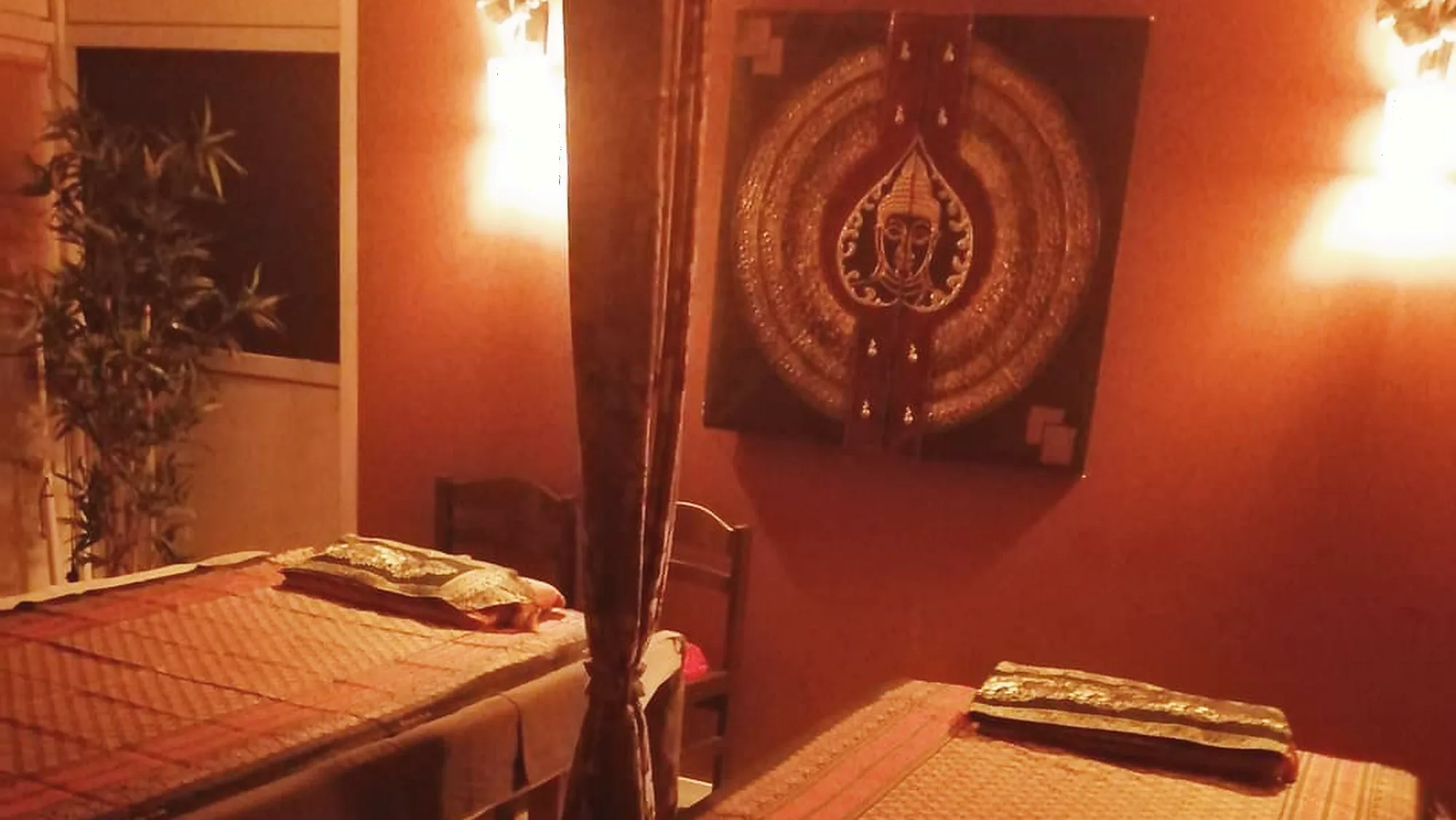 Behandlungsraum bei HomeSabay in Augsburg mit Thai-Liegen, Wandlampen und geschnitzter Wandarbeit